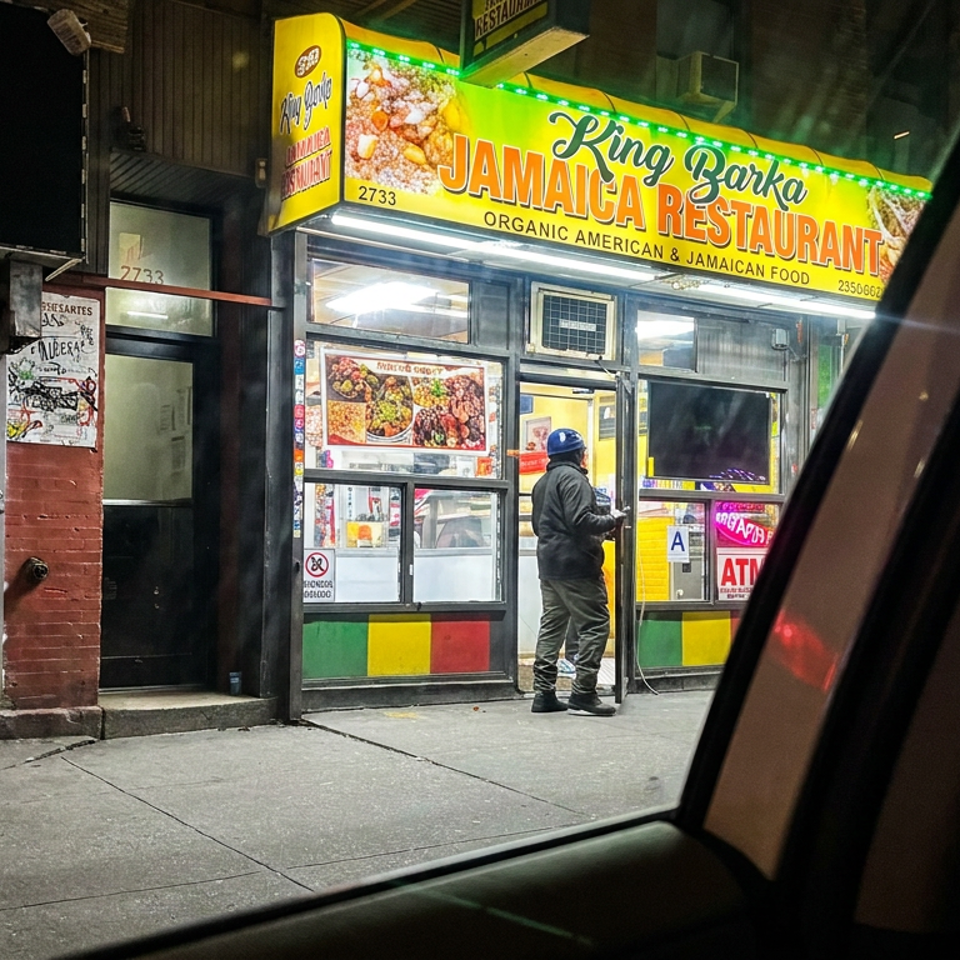 Nighttime storefront of King Zarka Jamaica Restaurant, featuring bright signage, food displays, and a customer at the entrance.