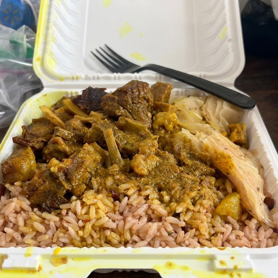 Takeout container filled with seasoned rice, saucy meat, fried plantains, and cabbage, with a black fork and water bottles nearby.